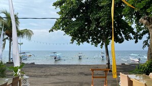 A beachside dining area with tables and chairs, overlooking the sea with boats in the background. - New Starlight Hotel & Resort (Buleleng)