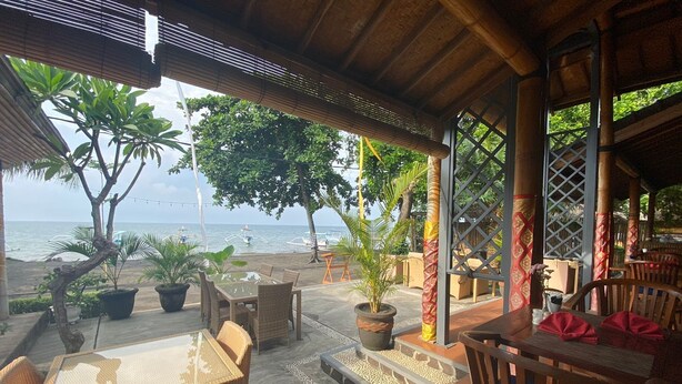 A covered outdoor seating area with wicker furniture, potted plants, and a view of the beach and ocean. - New Starlight Hotel & Resort (Buleleng)