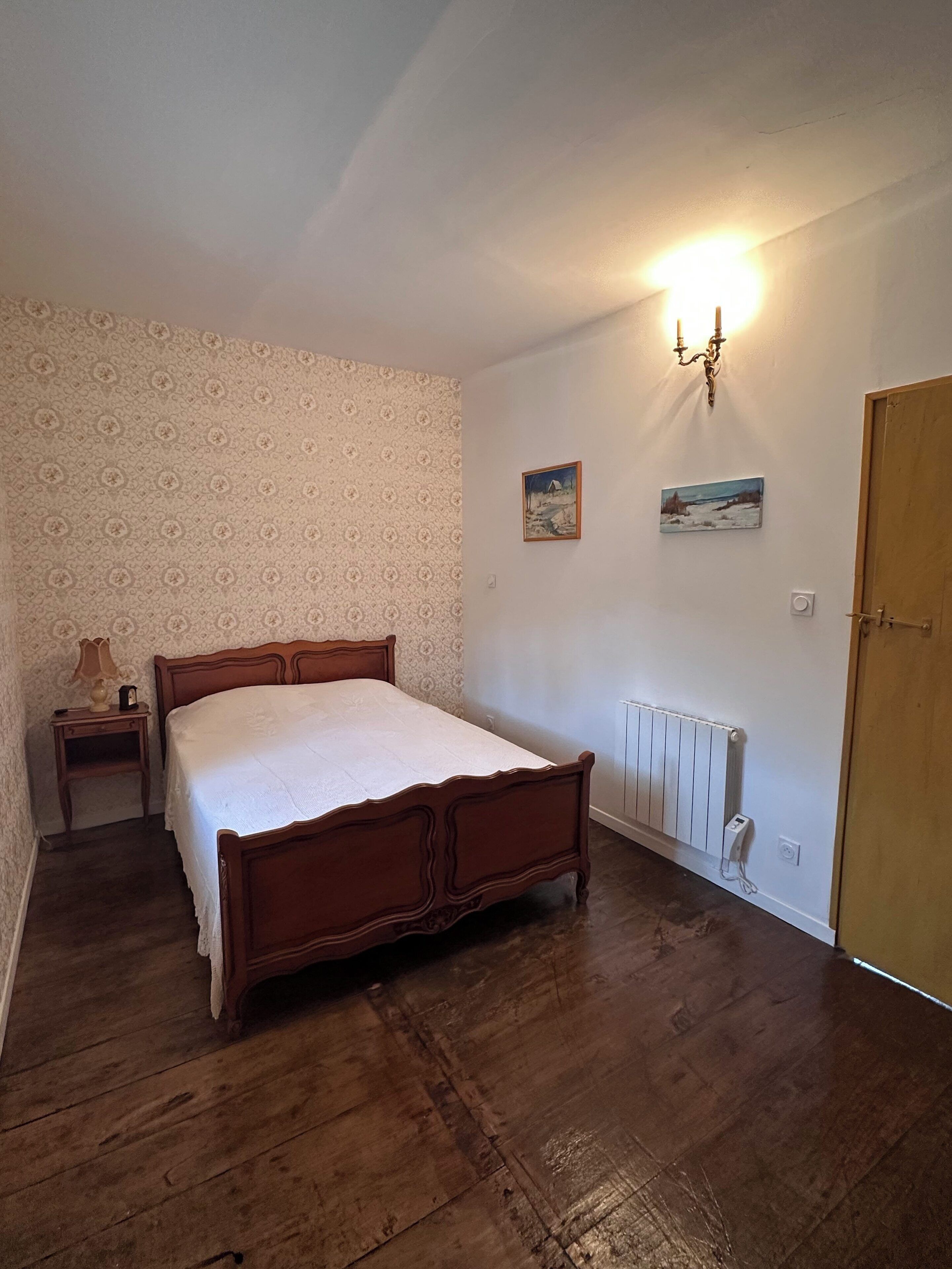 A bedroom with a wooden bed, a nightstand, a radiator, and two wall-mounted pictures.