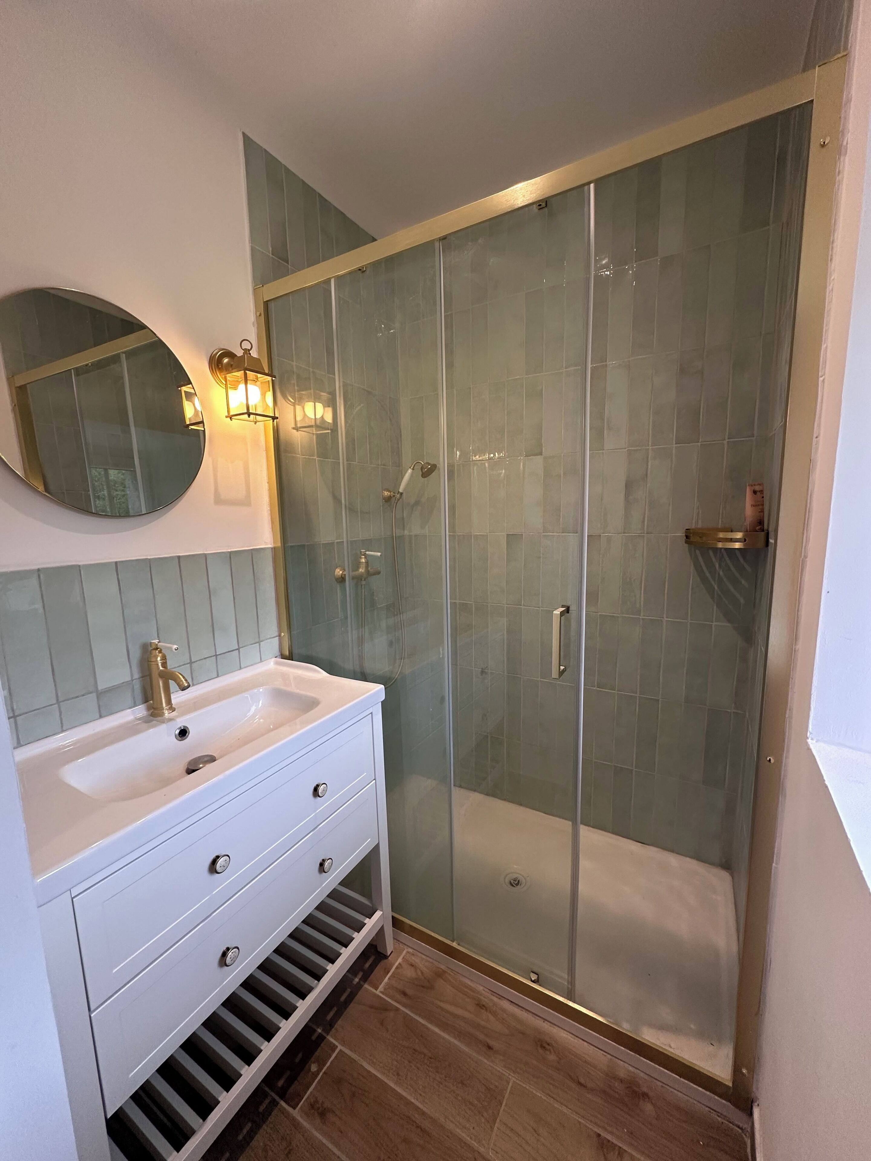 A modern bathroom with a glass-enclosed shower, a white vanity with a round mirror, and a tiled backsplash.