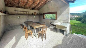 An outdoor kitchen area with a table and chairs, a window overlooking a green landscape, and a rustic wooden ceiling. - Authentic, rustic farmhouse in the heart of the Ariege Pyrenees (Saint-Lizier)
