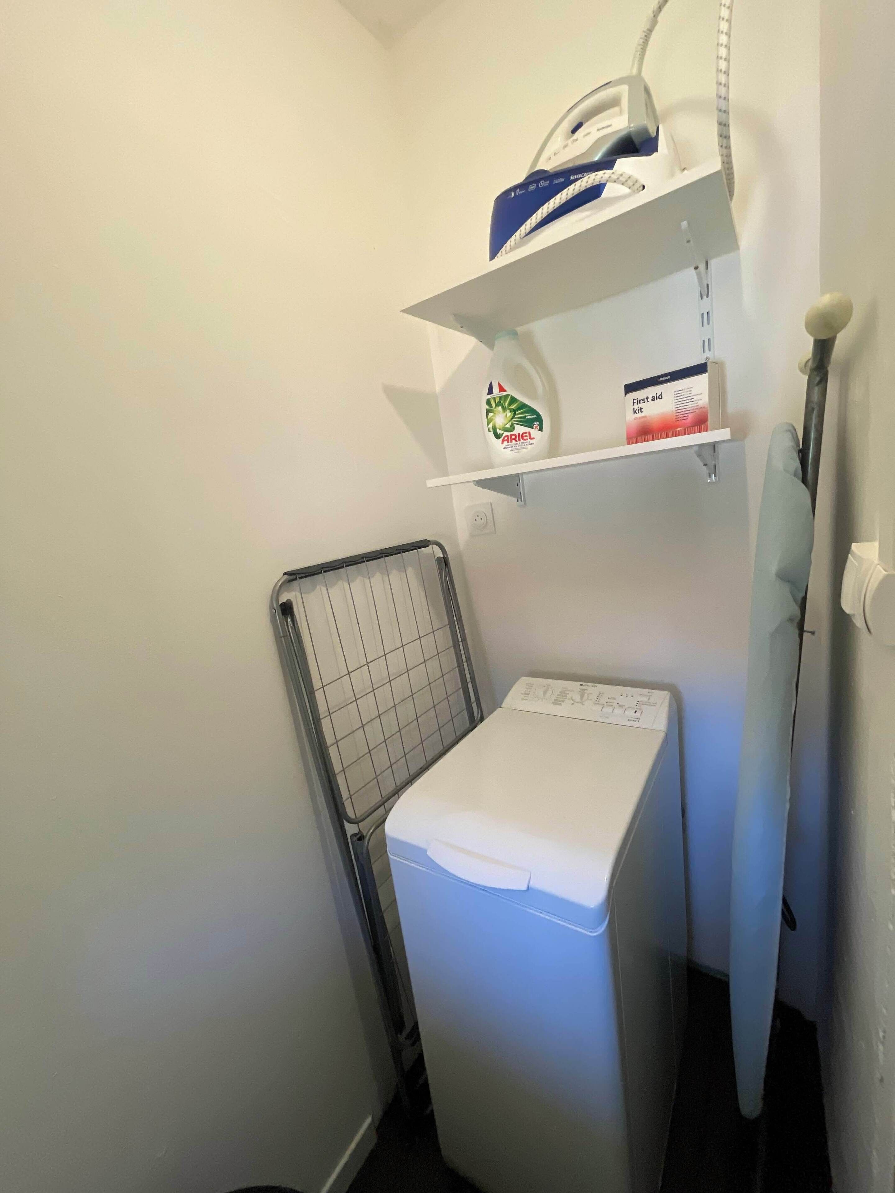 A laundry area with a washing machine, a drying rack, and shelves with cleaning supplies.