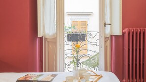 Una habitación con una cama, una mesa con bandeja, un florero y una ventana con cortinas.
