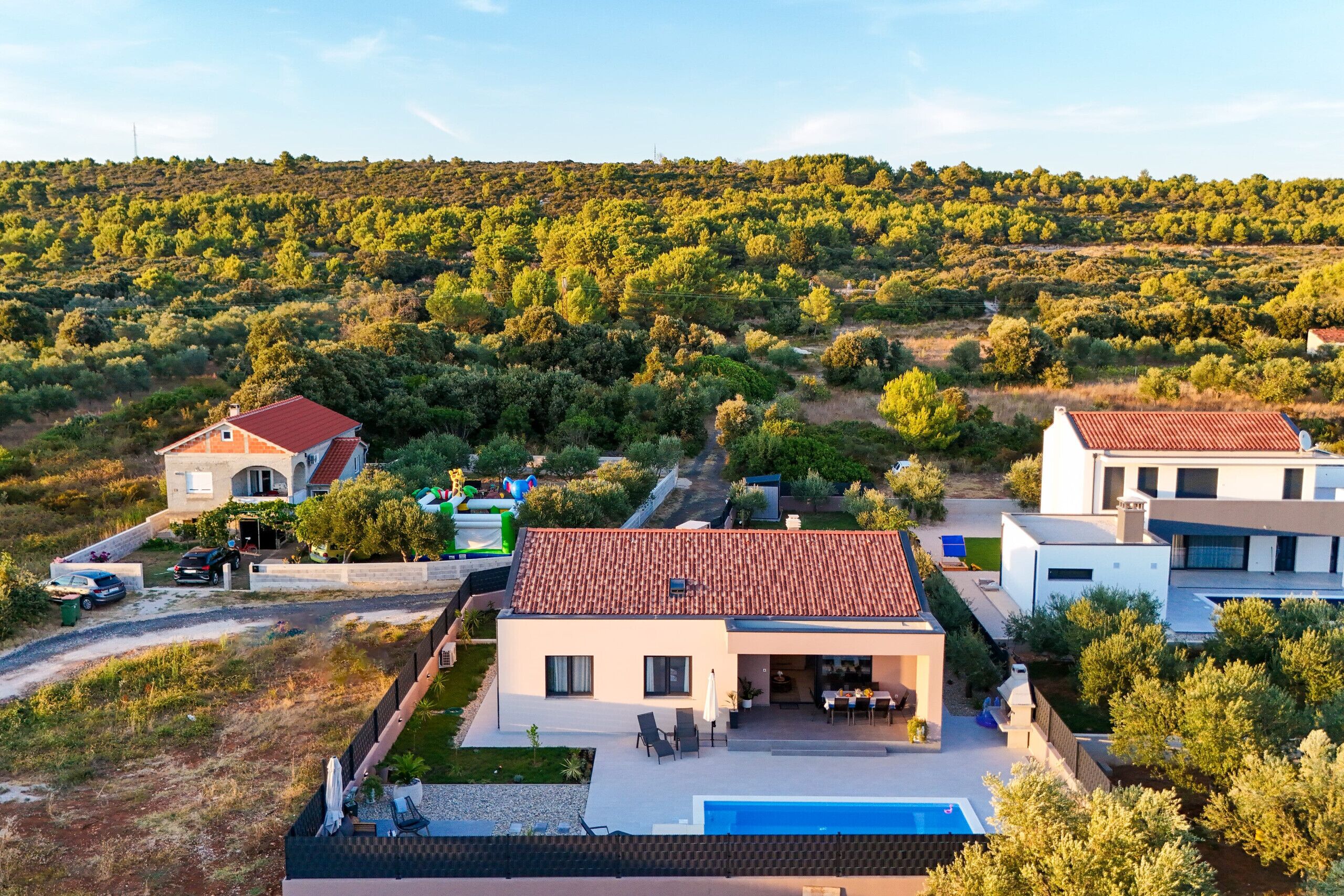 A modern villa with a swimming pool, surrounded by lush greenery and hills.