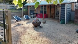 A covered outdoor area with a fire pit, two blue chairs, a red sofa, and a wooden fence. - Rainbow valley bunkhouse (Warrenbayne)