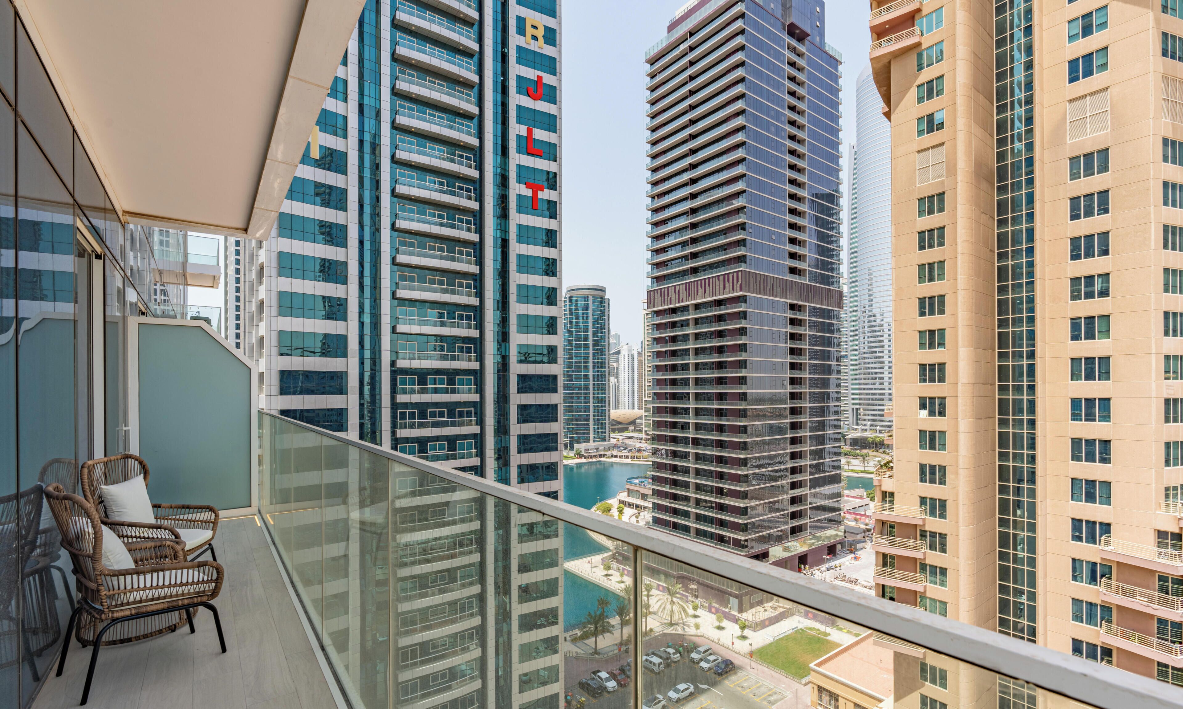A high-rise building with a balcony featuring wicker chairs and a glass railing.