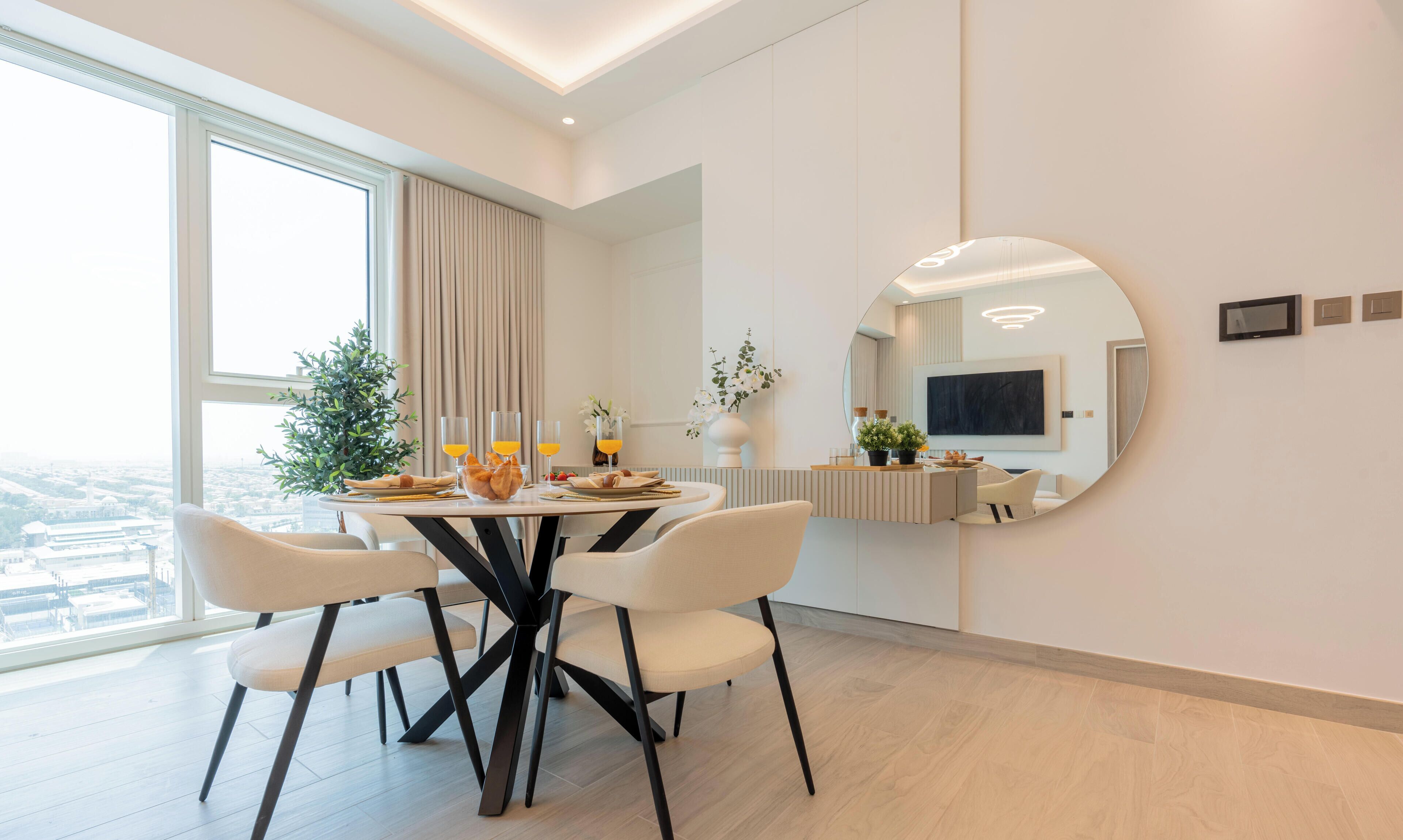 Un espace repas moderne avec une table ronde, des chaises blanches et une grande fenêtre agrémentée de rideaux.