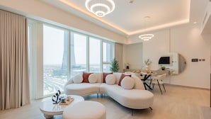 Una sala de estar moderna con un sofá en forma de L, una zona de comedor con una mesa redonda y vistas a la ciudad a través de amplias ventanas.