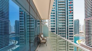 Un edificio alto con balcón de vidrio, sillas de mimbre y vista a un puerto deportivo.