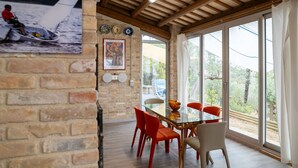 A dining area with a glass table and red chairs, a brick wall with a poster, and large windows with a view of greenery. - Wonderful  villa with WIFI, private pool, A/C, hot tub, patio, pets allowed and panoramic view (Città Sant'angelo)