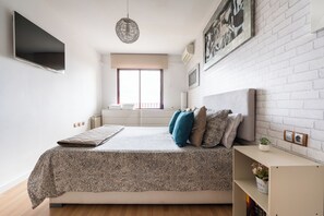 A bedroom with a bed, a TV, a window, and a white brick wall.
