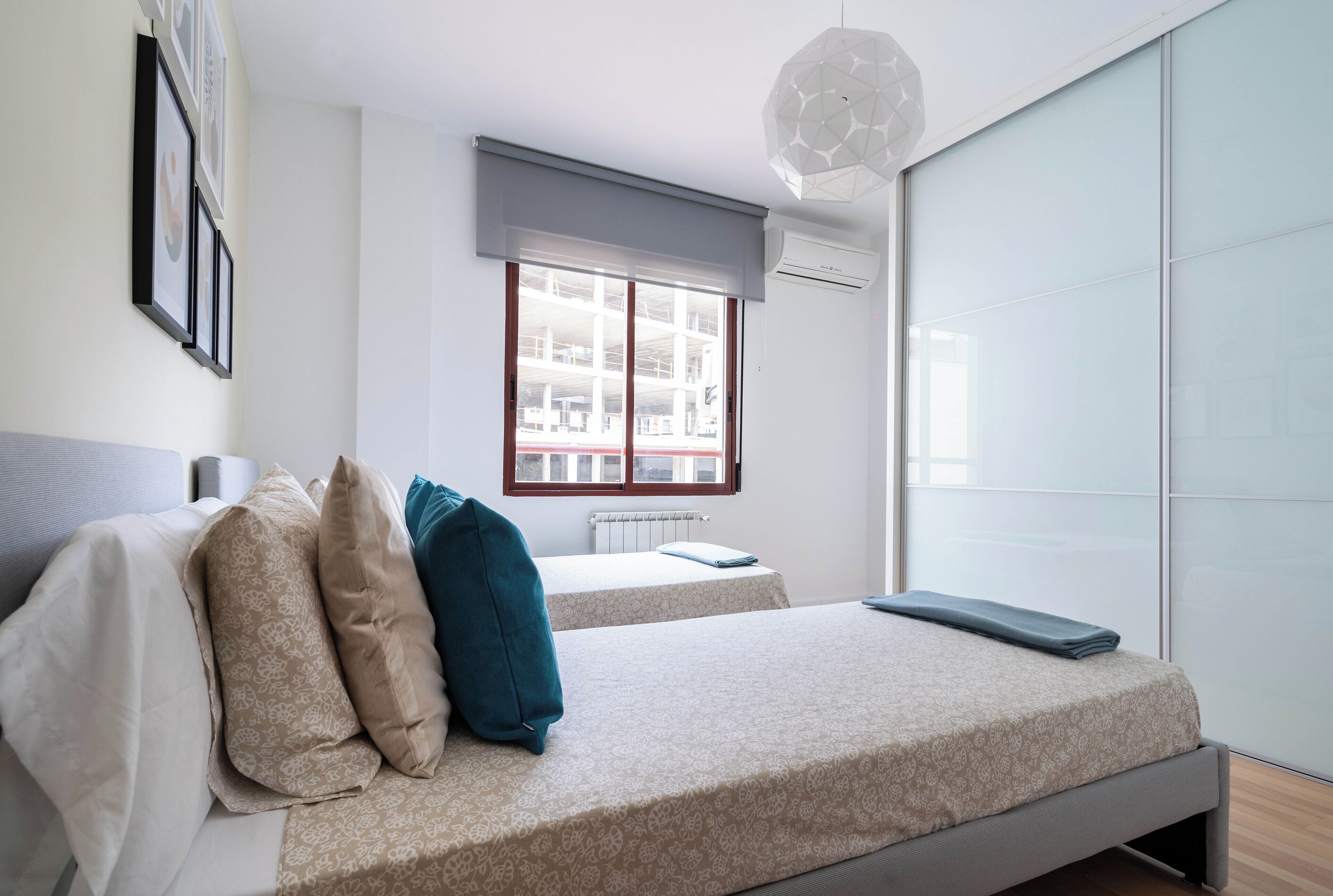 Un dormitorio moderno con dos camas, un ventanal grande y una lámpara de techo.
