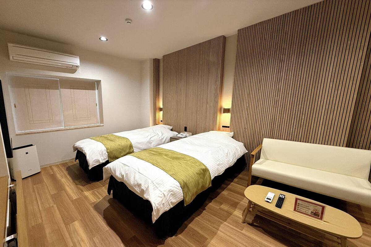 Ein Hotelzimmer mit zwei Betten, einem Sofa, einem kleinen Tisch und einer Wandklimaanlage.