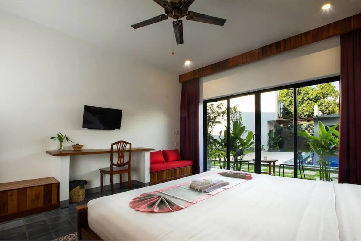 A hotel room with a bed, a desk, a chair, a TV, and a large window with a view of the outdoors.
