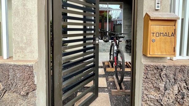 A gated entrance with a metal gate, a wooden mailbox labeled "TUMALA," and a bicycle parked outside.