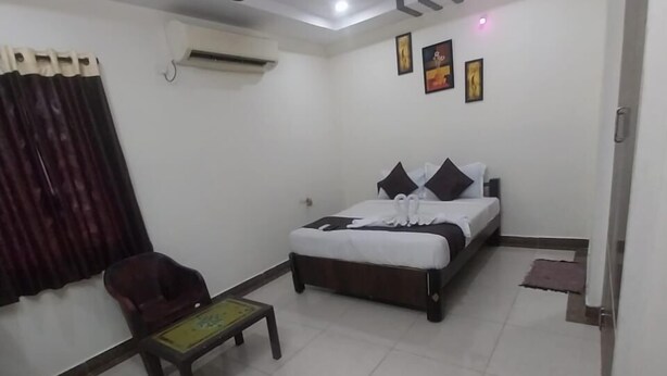 A hotel room with a bed, a chair, a small table, a ceiling fan, and an air conditioning unit. - Smart Stay Rooms (Vijayawada)