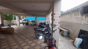 A covered parking area with a tiled floor, several parked motorcycles, and a few cars. - Smart Stay Rooms (Vijayawada)