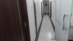 A narrow, tiled hallway with a wooden door on the left and a glass door with a push bar on the right. - Smart Stay Rooms (Vijayawada)