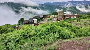 Un entorno rural con un pequeño conjunto de edificios rodeado de abundante vegetación y montañas.