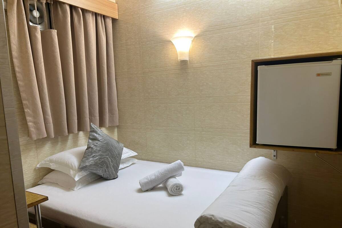 A hotel room with a bed, a wall-mounted light, a whiteboard, and a window with curtains.