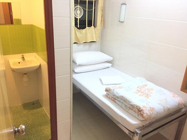 Una habitación pequeña con cama individual, un lavamanos blanco y una ventana con cortina.