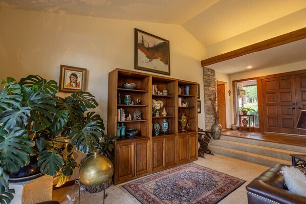 A spacious living room with a large wooden bookcase, a potted plant, and a colorful rug.