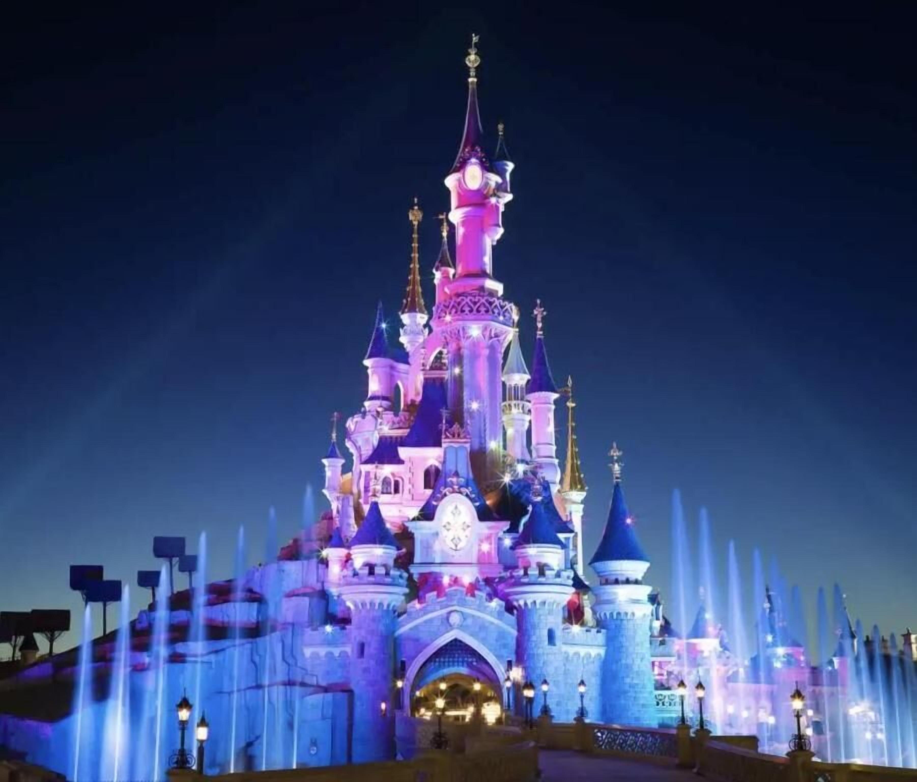 A castle with multiple towers and a large entrance, surrounded by water fountains.
