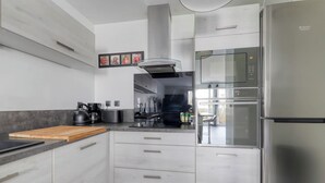 A modern kitchen with stainless steel appliances, a wooden cutting board, and a view into the dining area. - 123home -The Outlet (Serris)