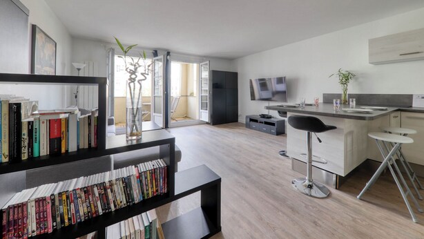 A modern living room with a bookshelf, a dining area with a bar, and a TV. - 123home -The Outlet (Serris)
