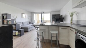 A modern kitchen with a central island, bar stools, and a built-in washing machine. - 123home -The Outlet (Serris)