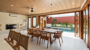 Un vaste espace dédié à la salle à manger, avec une table et des chaises en bois, un ventilateur de plafond et une vue sur une piscine.