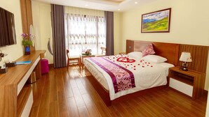 Habitación de hotel con cama, mesita de noche, escritorio, silla y ventana con cortinas.