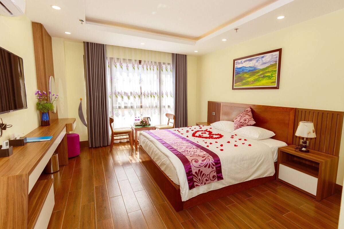 A hotel room with a bed, bedside table, desk, chair, and a window with curtains.