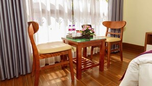 Una habitación con dos sillas de madera, una mesita con un jarrón de flores y una ventana con cortinas de encaje y adornos florales.