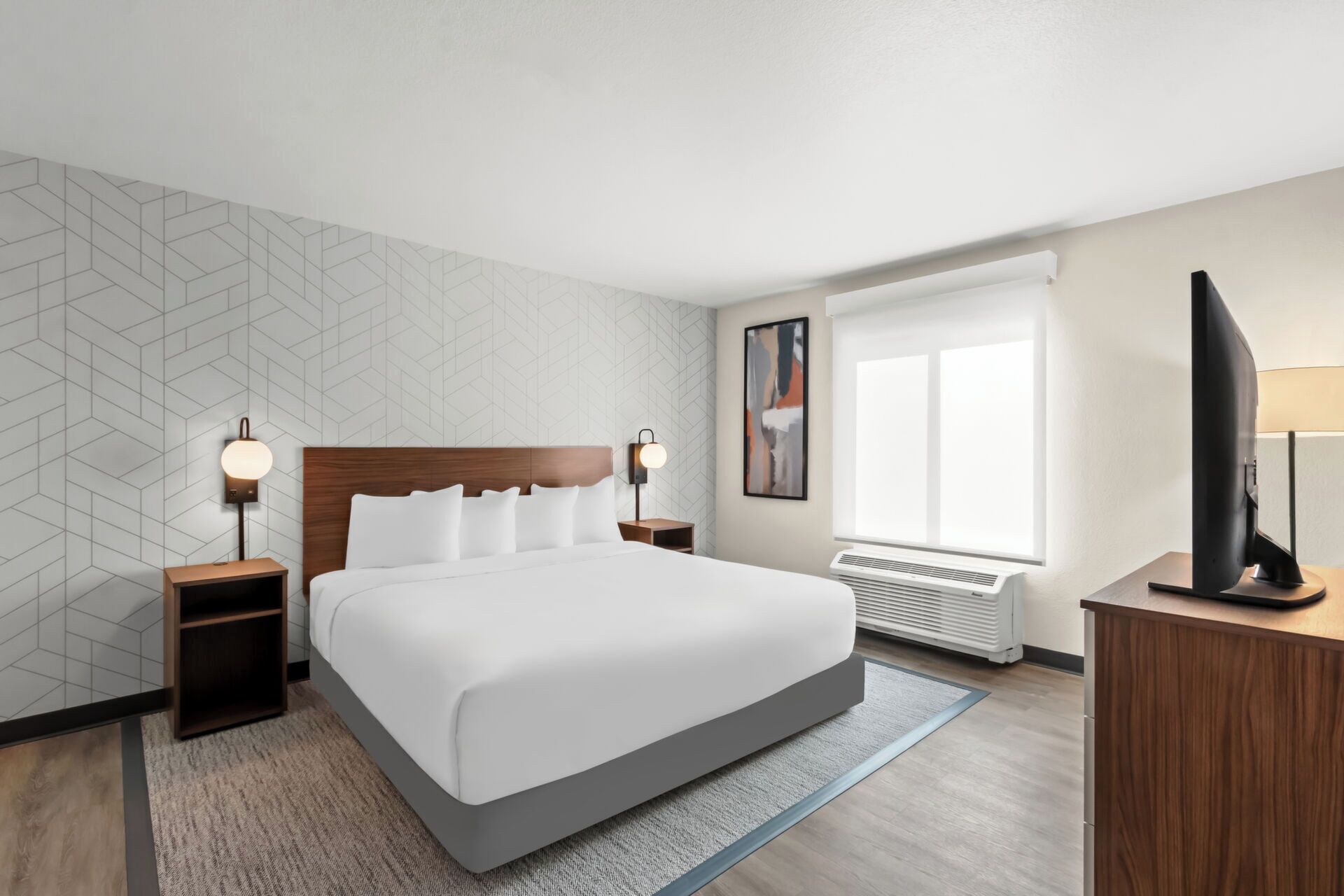 A modern hotel room with a large bed, two bedside tables with lamps, a flat-screen TV, a large window, and a radiator.
