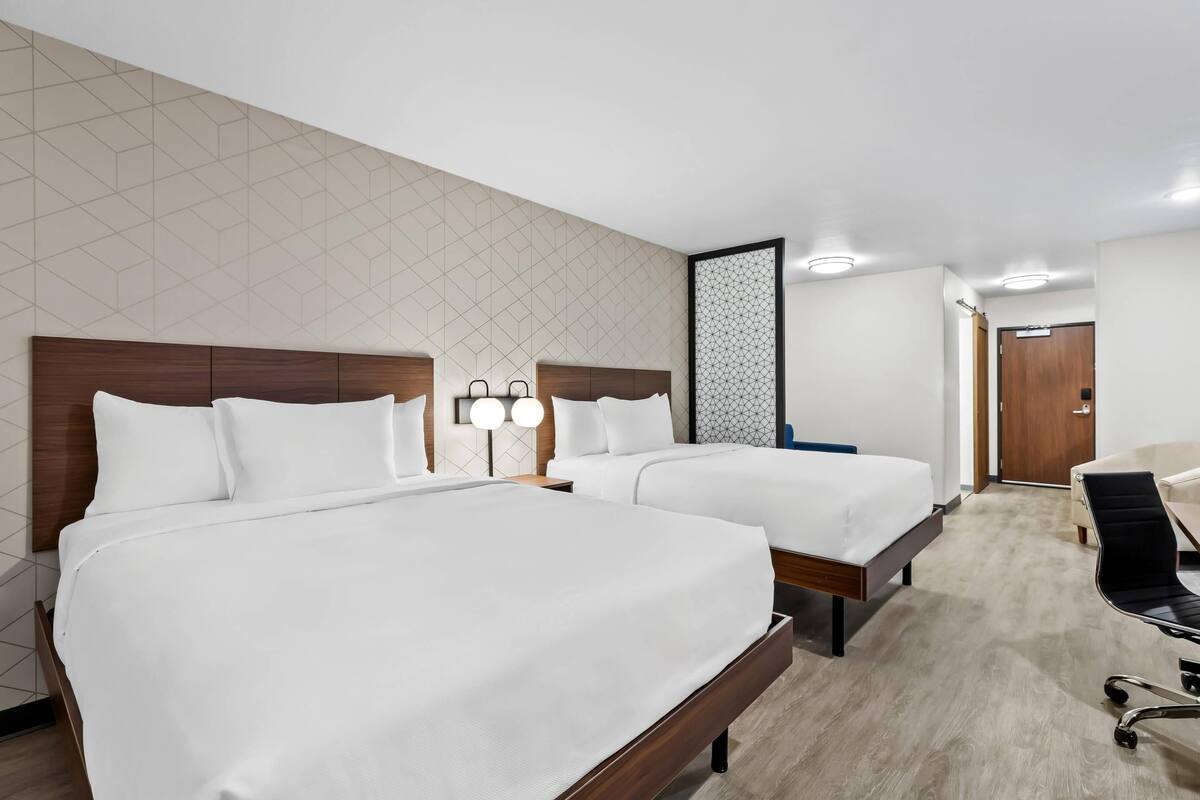 A hotel room with two beds, a desk, and a chair.