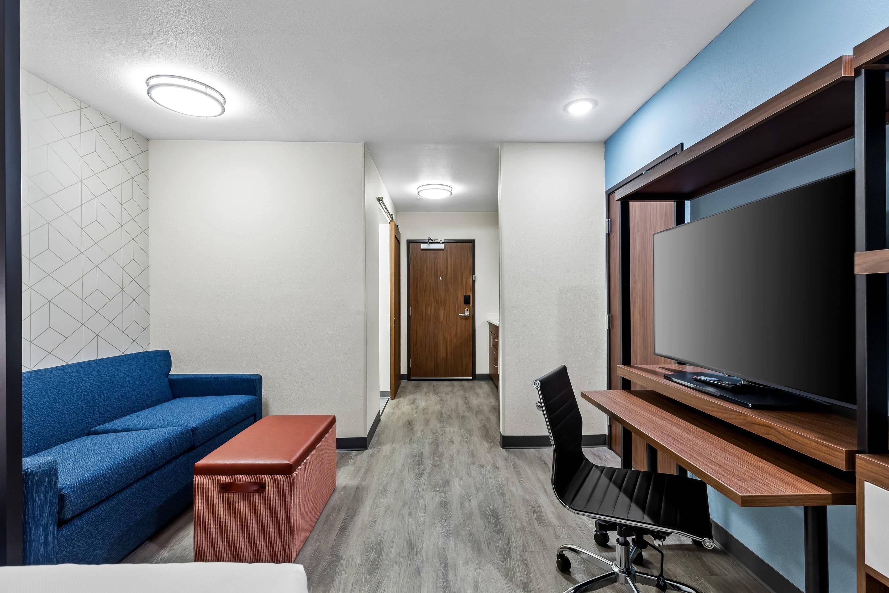 A modern room with a blue sofa, a wooden desk with a TV, a red storage unit, and a patterned wall.