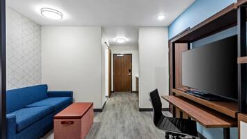 A modern room with a blue sofa, a wooden desk with a TV, a red storage unit, and a patterned wall.