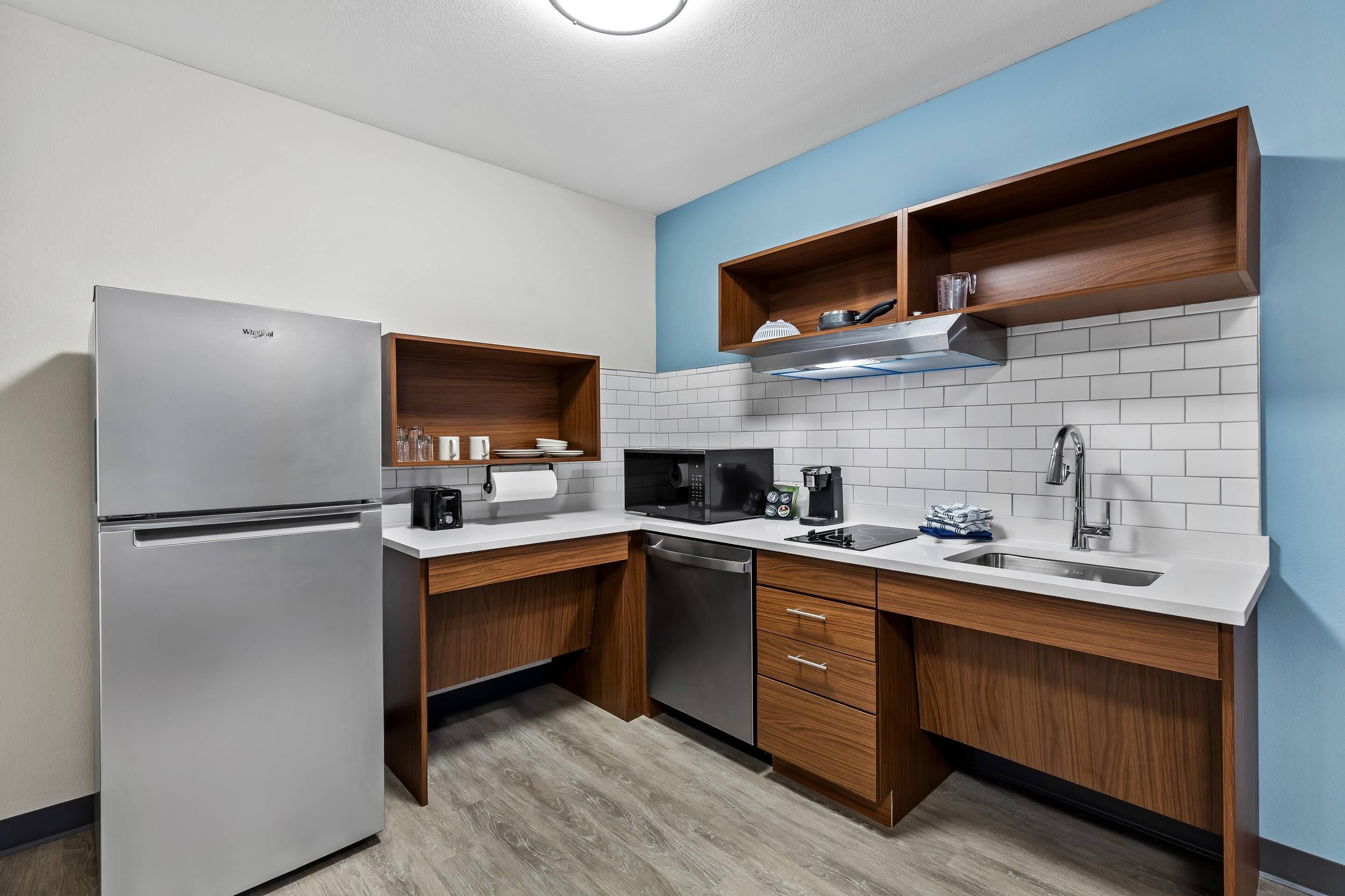 A modern kitchen with a stainless steel refrigerator, a microwave, a coffee maker, and wooden cabinets.