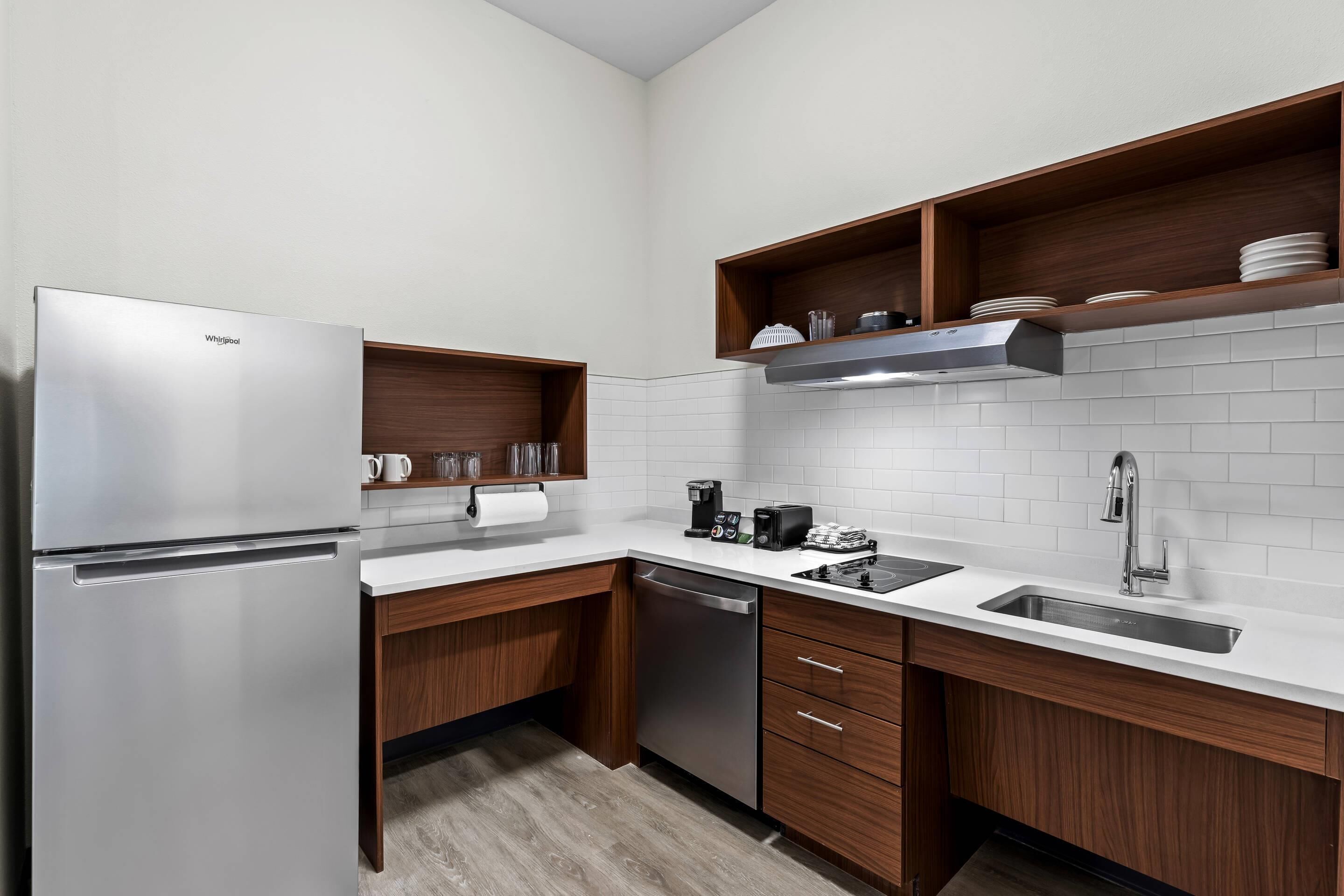 A modern kitchen with a stainless steel refrigerator, wooden cabinets, a built-in oven, and a stainless steel sink.