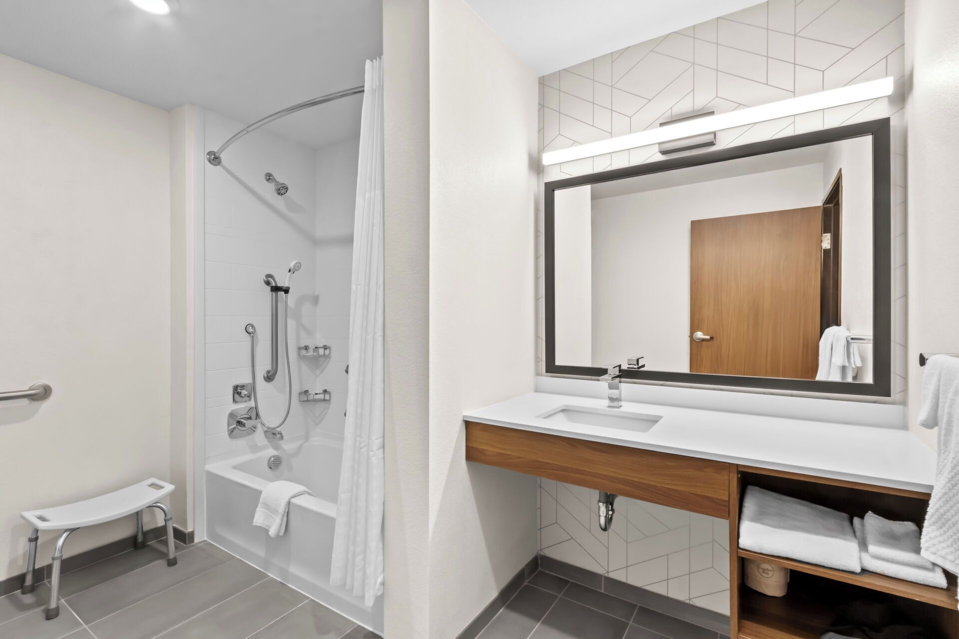 Ein modernes Badezimmer mit begehbarer Dusche, einer Badewanne, einem Waschtisch mit Spiegel und einem Handtuchhalter.