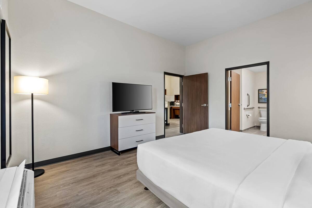A hotel room with a large bed, a flat-screen TV, a desk with a lamp, and a wardrobe.