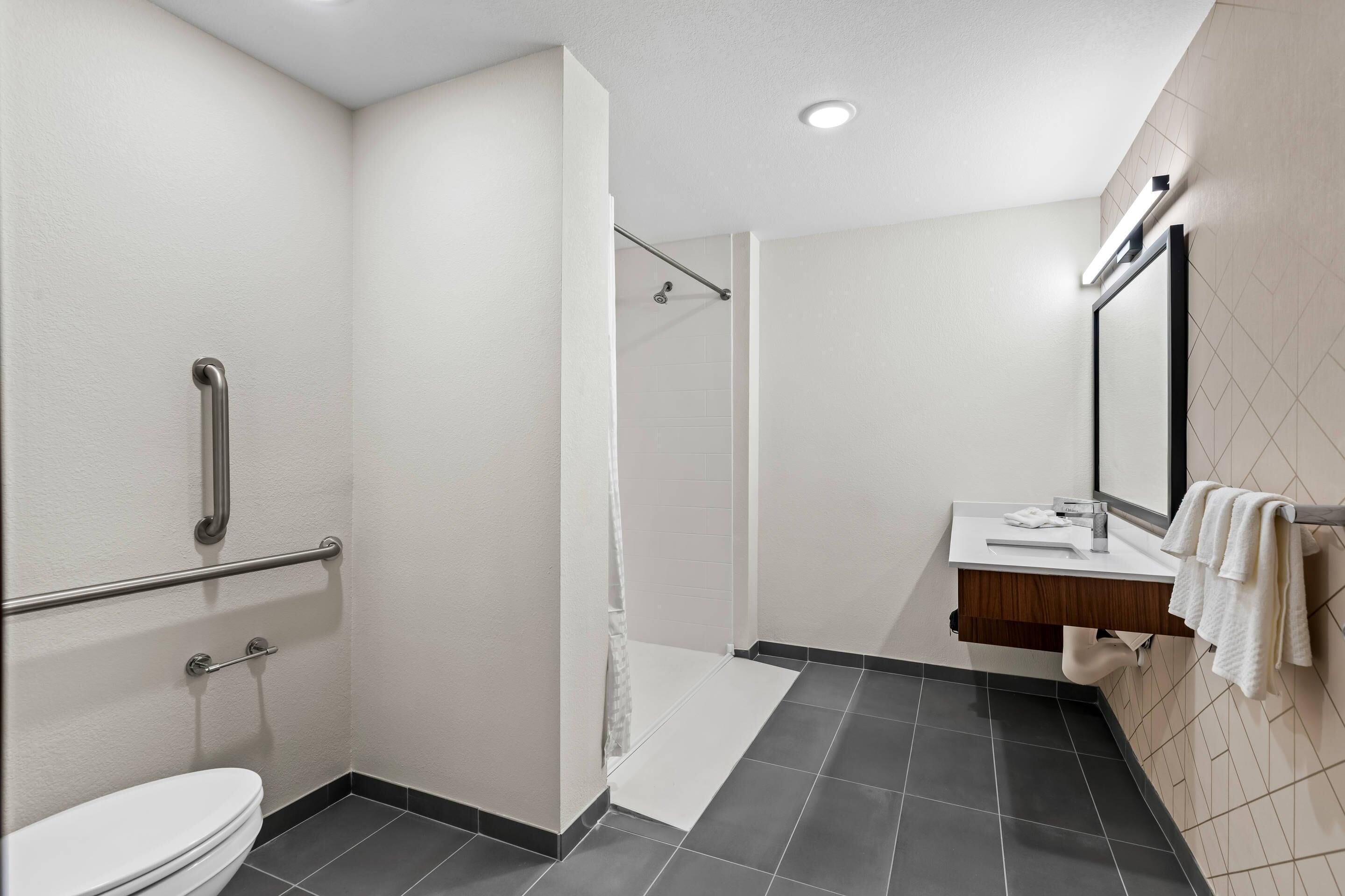 A modern bathroom with a toilet, a shower with a glass door, a vanity with a mirror, and a towel rack.