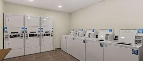 A laundry facility with multiple washing machines and dryers, arranged in rows.