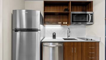 A compact kitchen with a stainless steel refrigerator, a microwave, a coffee maker, and wooden cabinets.