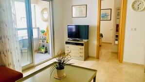 A living room with a TV on a stand, a potted plant on a table, and a view of the outside through a sliding door. - Centric and Full of Light! Casa Alicia Altea (Altea)