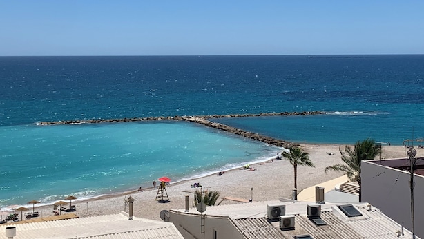 A beach view with a clear sky, a rocky breakwater, and a sandy beach with umbrellas and palm trees. - Centric and Full of Light! Casa Alicia Altea (Altea)
