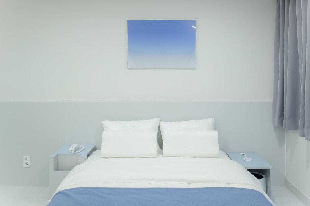 A hotel room with a bed, two bedside tables, a nightstand, a telephone, and a window with curtains.