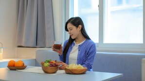 A person sitting at a table with bowls of fruit and a drink, in a room with a window and curtains. - Anook Air Hotel Jinju (Jinju)