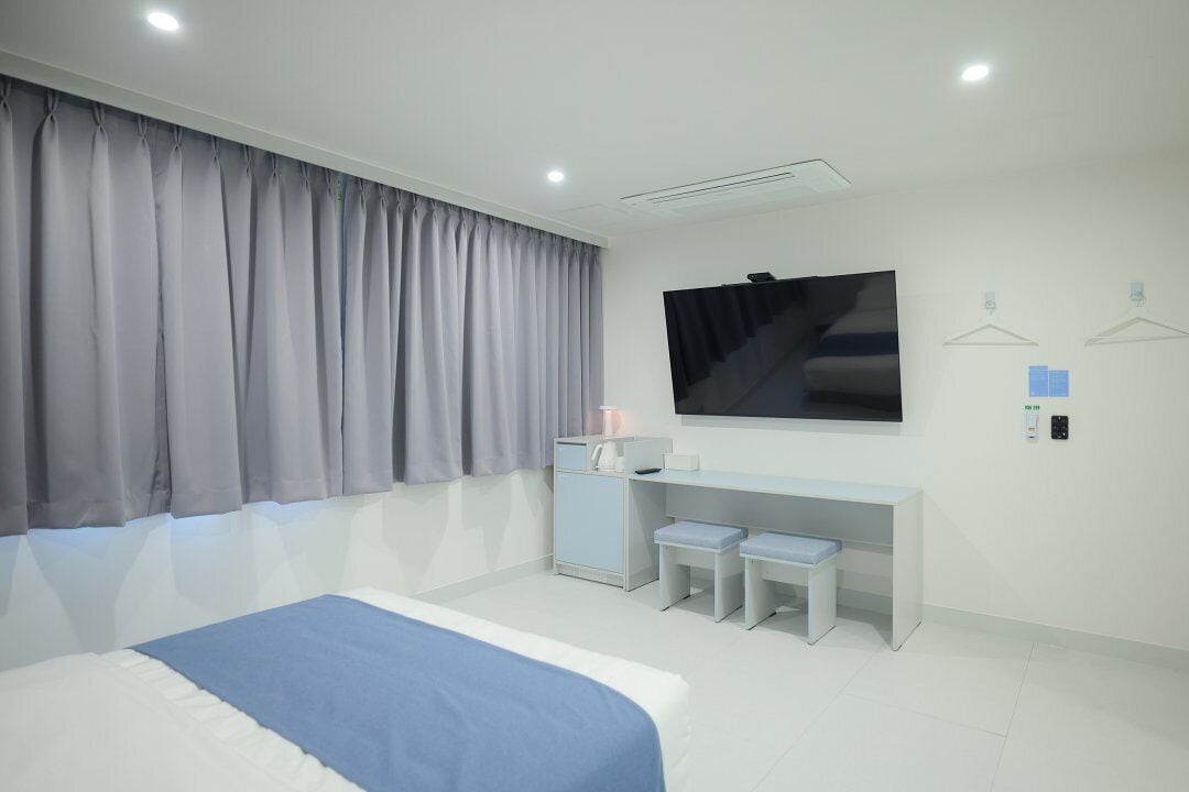 A modern hotel room with a large bed, a desk with two chairs, a flat-screen TV, and a wardrobe.